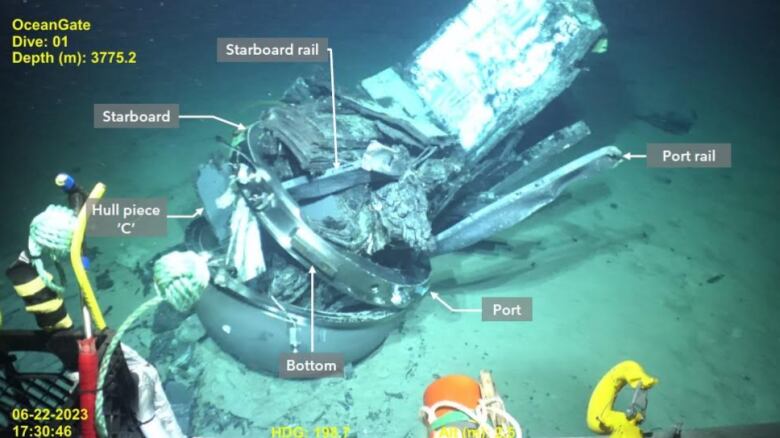 A damaged, silver submersible sitting on the bottom of the ocean floor. 