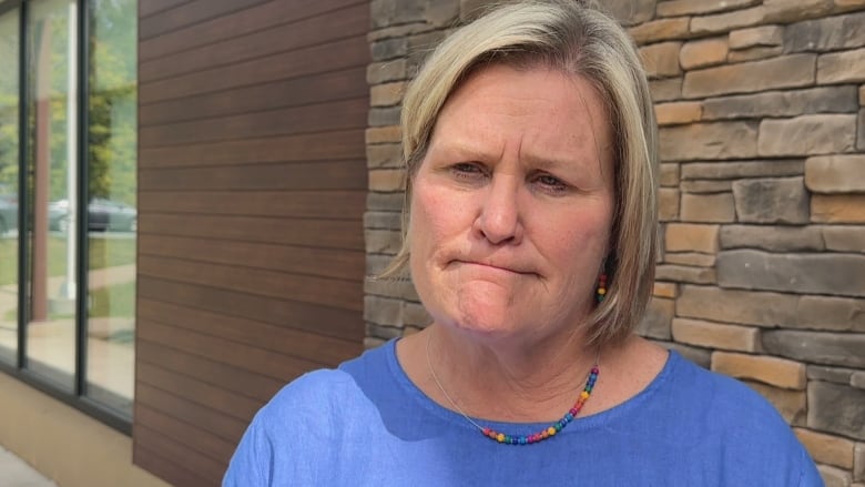 Woman in blue top stands near a wall