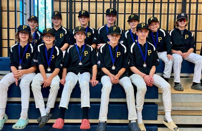 A team of smiling boys wearing baseball uniforms sit on bleachers inside a gym.