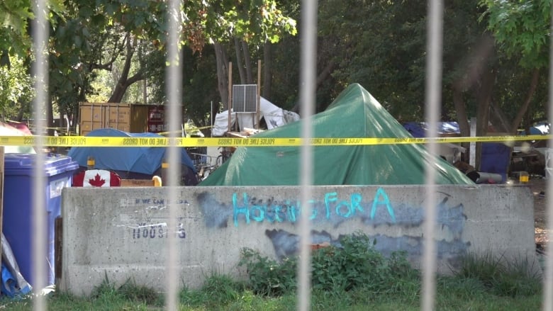 Tents surrounded by police tape are shown beyond a fence.