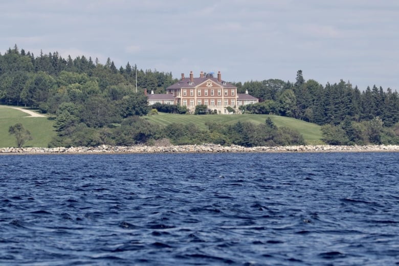 A large brick home with a large grassy area leading to the water is shown.