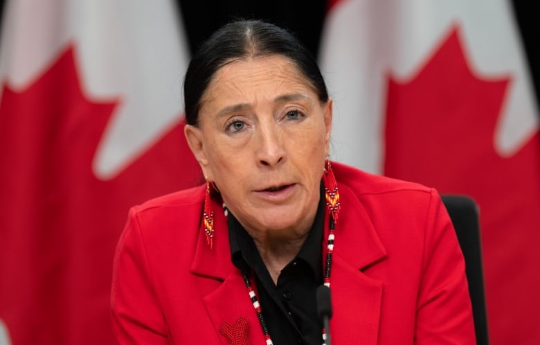 woman in red suit speaks at a news conference