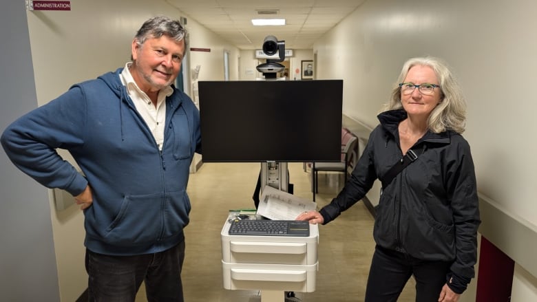 Two people stand with a telemedicine unit which is a TV monitor with a camera and a laptop 