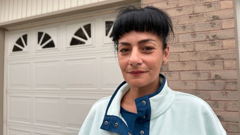 A woman stands smiling in front of a garage.