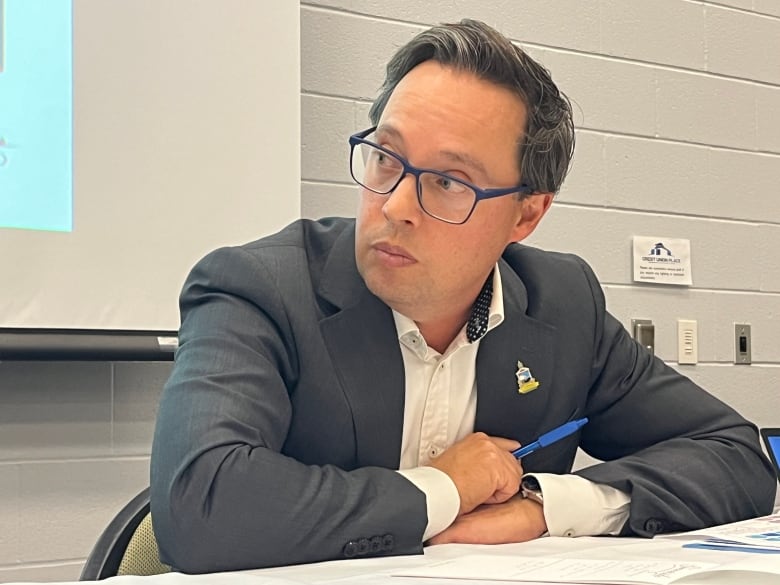 A man in a suit, but no tie, listens carefully during a public meeting. 