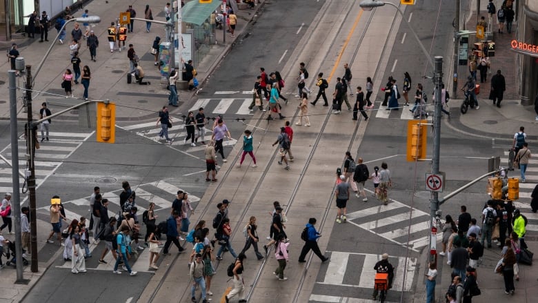 An aerial shot showing many people crossing the road in all directions in a city. 