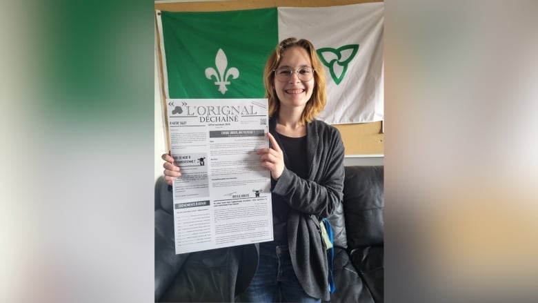 A young woman with glasses holding a newspaper.