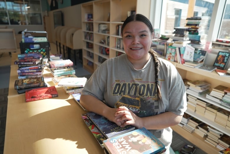 A woman stands between a row of book shelves in a school library.