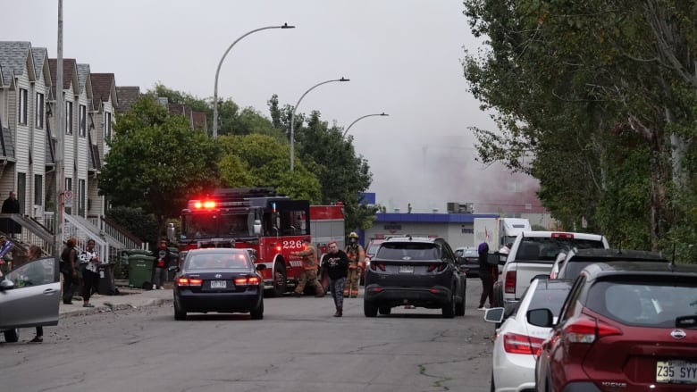 smoke in background of firetrucks and people in neighbourhood