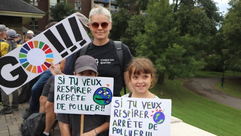 A woman wearing sunglasses and her two children, a boy and a girl, hold signs at the climate march in Quebec City. 