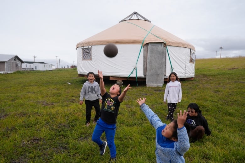 Children playing on the tundra in front of a yurt.