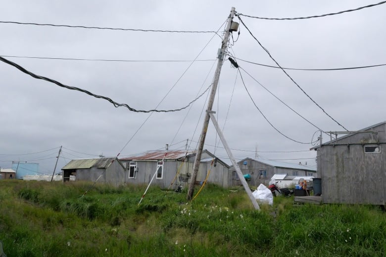 A power pole leans over near some dilapidated homes.