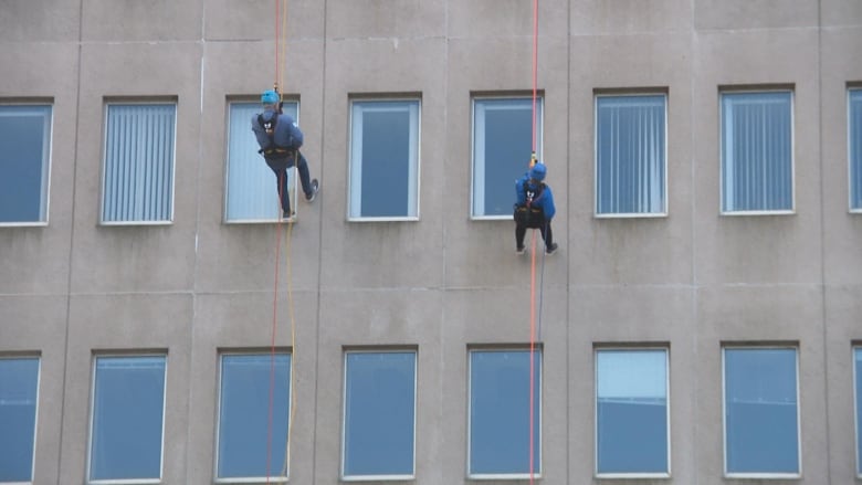 Two people rappelling down the side of a building.