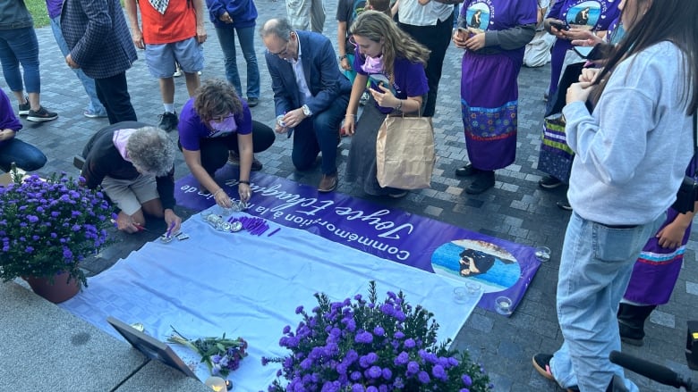 People wearing purple t-shirts gather around a memorial for Joyce Echaquan.