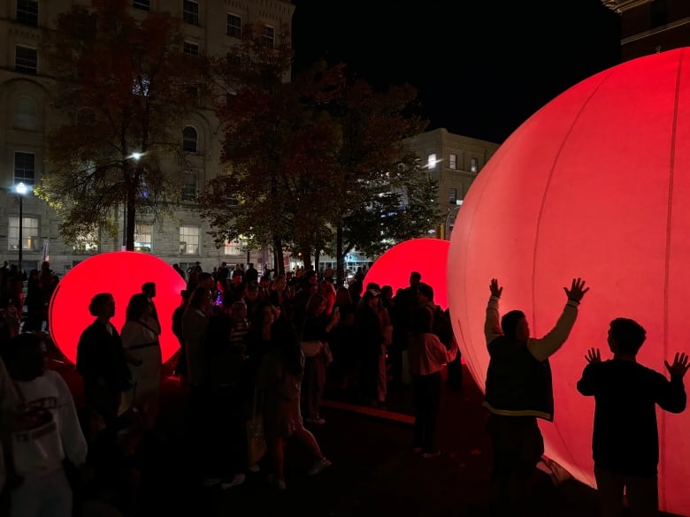 People walk around giant glowing balls at night during an arts festival. 