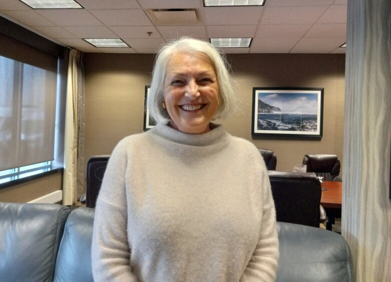 Woman with short white hair, smiling, wearing a white sweater.