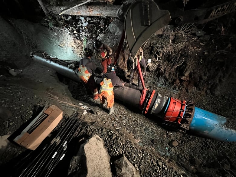 Workers wearing high-vis vests work on a pipe in the ground.