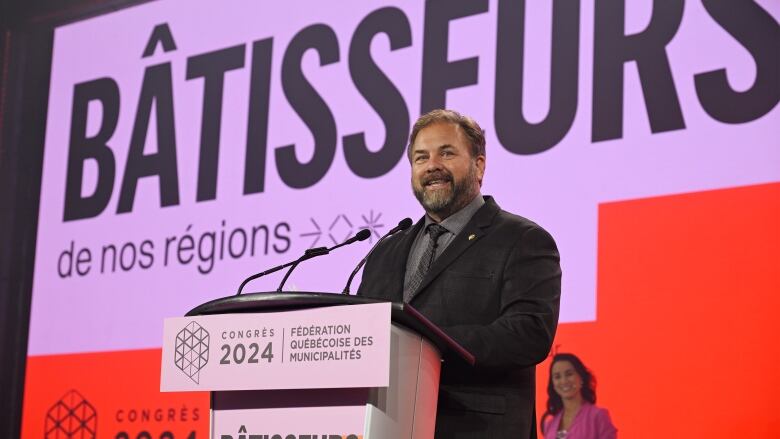 A brown-haired white man in a black suit speaking at a podium at the 2024 Fdration Qubcoise des Municipalits congress.