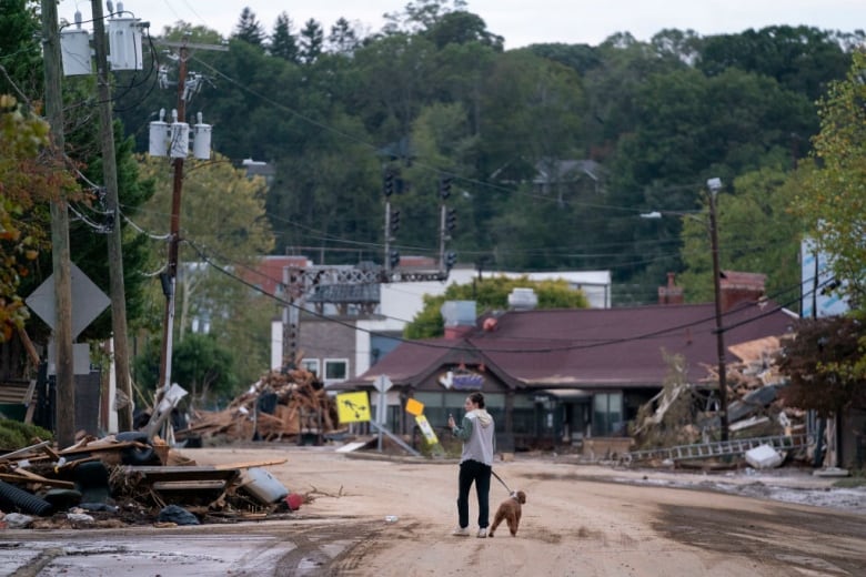 A woman walks her dog along a street where buildings were badly damaged in a hurricane.