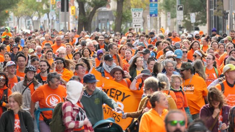 A crowd of people walk in a march wearing orange.