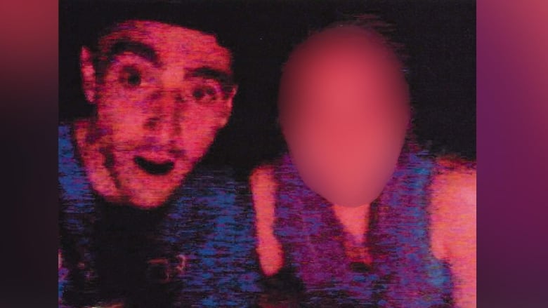 A man wearing a dark cap poses with a woman whose face is blurred.