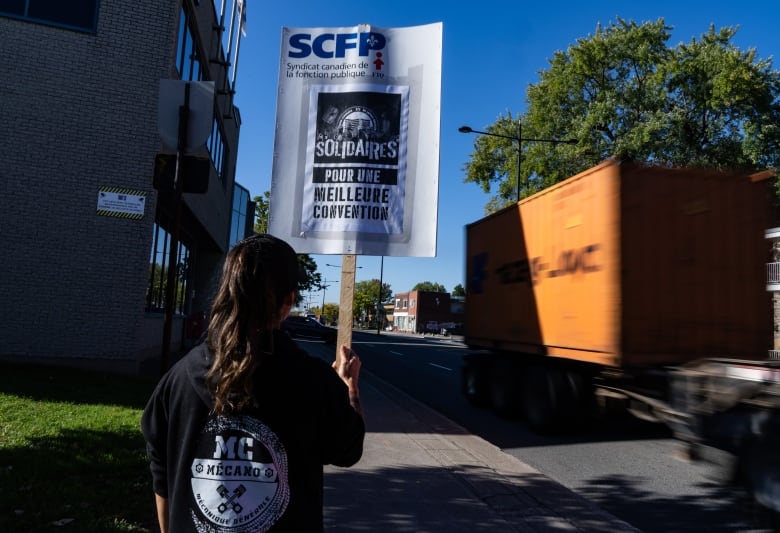 Worker holds up protest sign near a delivery truck heading to the port. 