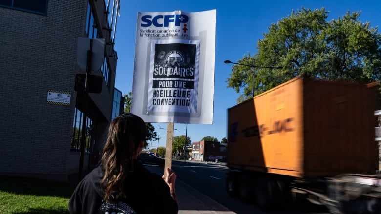 Worker holds up protest sign near a delivery truck heading to the port. 