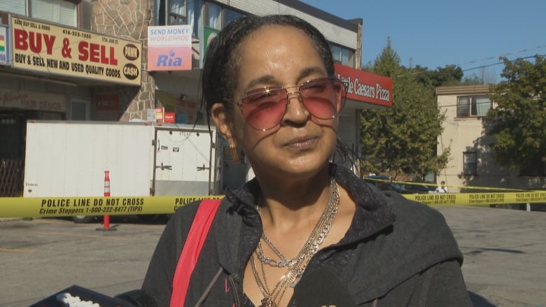 A middle aged man wears sunglasses and talks to reporters in front of police tape on a city street