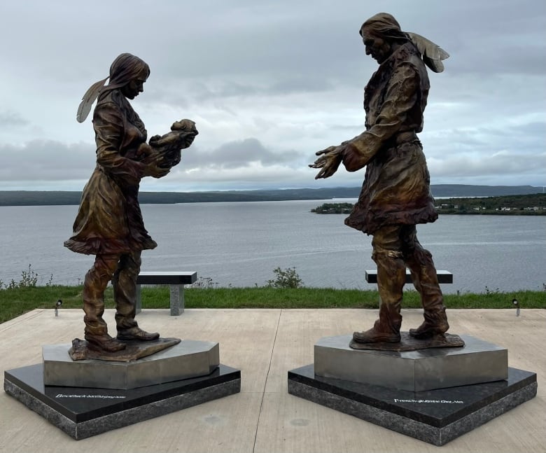 Two bronze statues. One shows a woman holding a baby, while the other shows a man with his arms stretched out toward the woman.