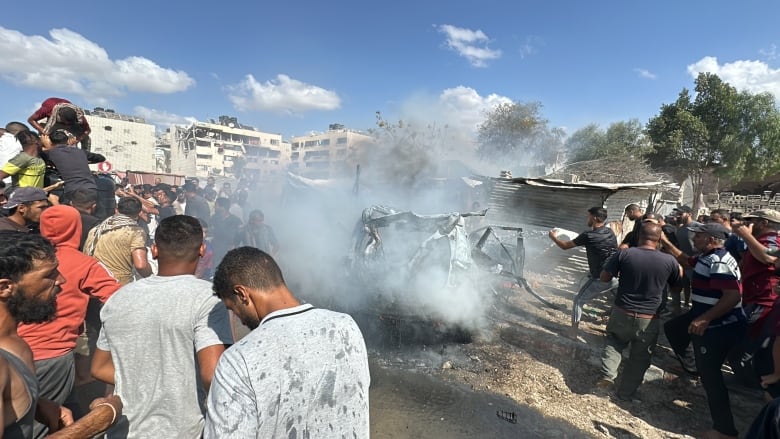 People stand around as some try to put out a car on fire.