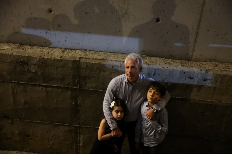 A man  stands with his arms around two children