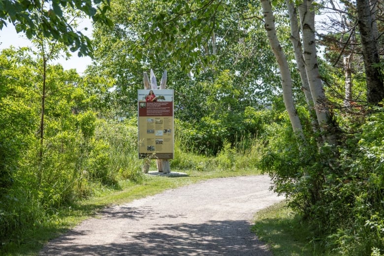 Sign along a gravel path in wooded area.