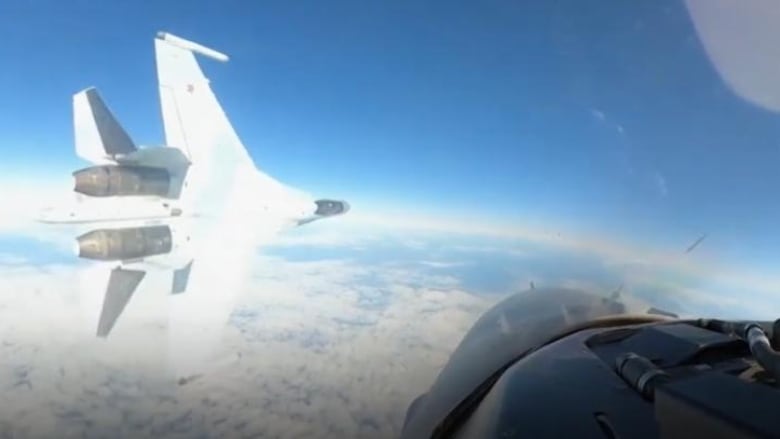 A fighter jet is seen flying by, through the window of another aircraft.