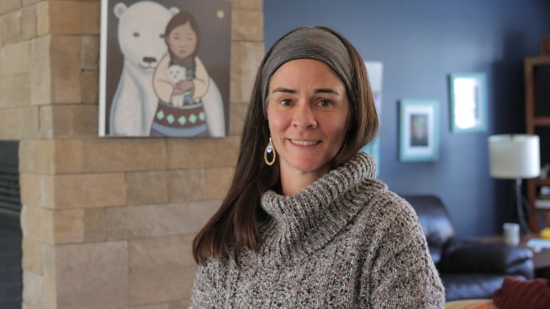 A person with long hair is wearing a turtleneck sweater, earrings and a headband. 