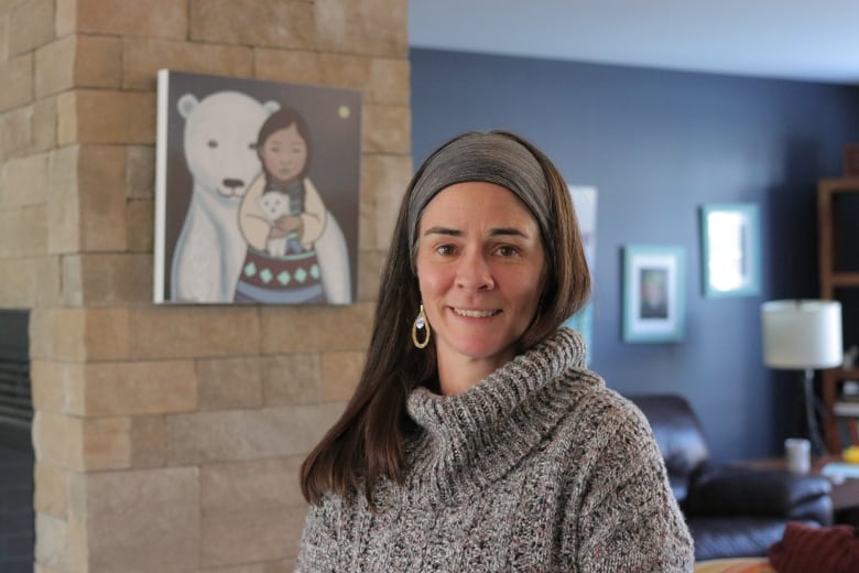 A person with long hair is wearing a turtleneck sweater, earrings and a headband. 