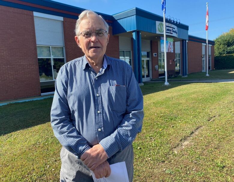 A man looks at the camera, standing in front of a school 