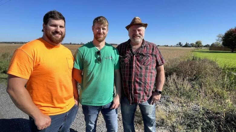 Three men stand in a farm field.