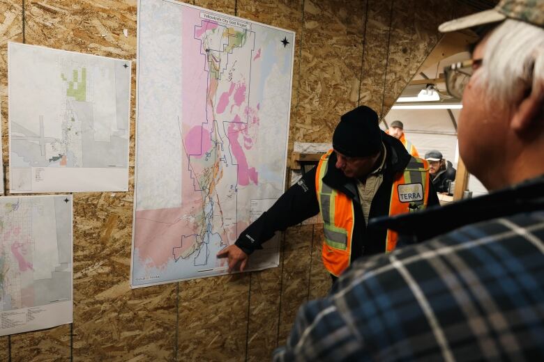 Man in construction vest points to map of mining areas in Yellowknife as spectators watch