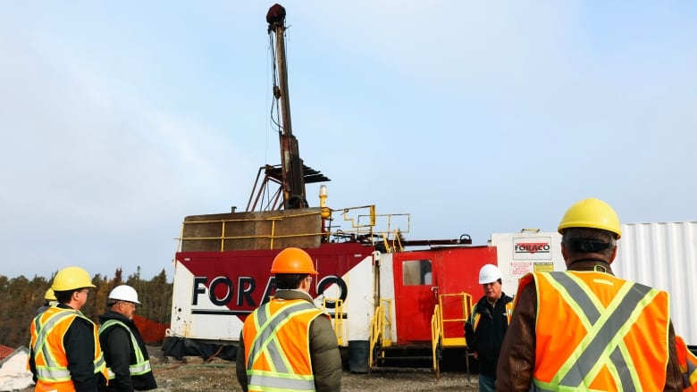 A group of men in construction vests stand in front of a drill for mining 