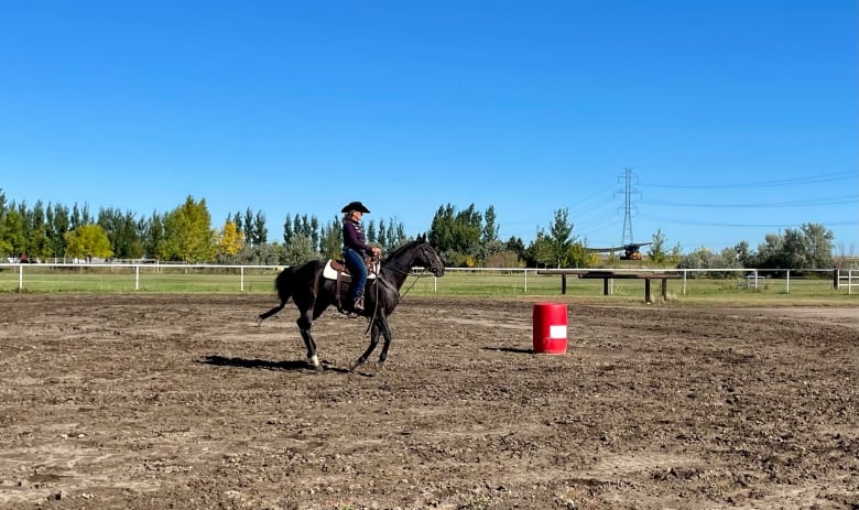 A woman with a cowboy hat rides a horse in an outdoor arena. 