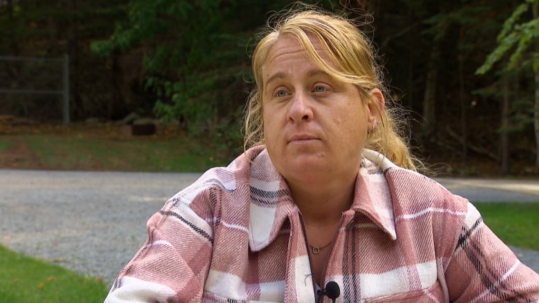 A woman sits in a pink jacket and looks at the camera.