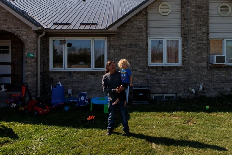 Grandfather holds his grandson in front of a home, on a sunny day.