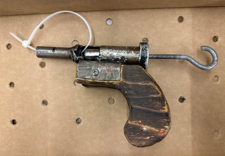 A crude firearm made of wood and metal with a zip tie through the barrel. 