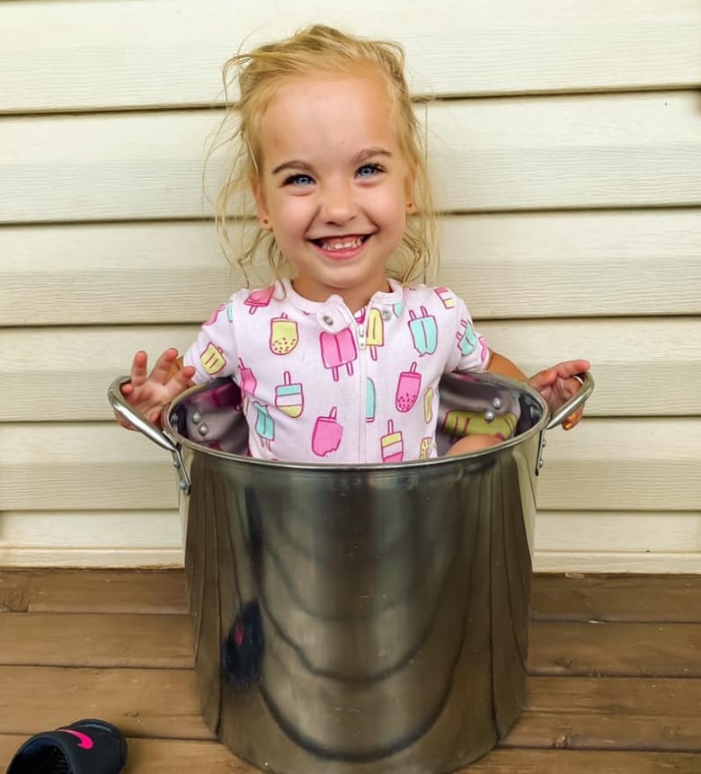 Little smiling blond girl in pink outfit sitting in a large metal lobster pot, smiling