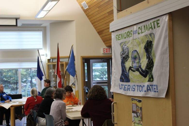 A banner that says Seniors for Climate on the right, with people talking at a table in the background to the left.