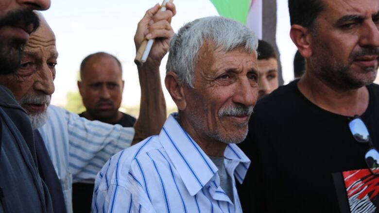 A father stands around mourners at his son's funeral.