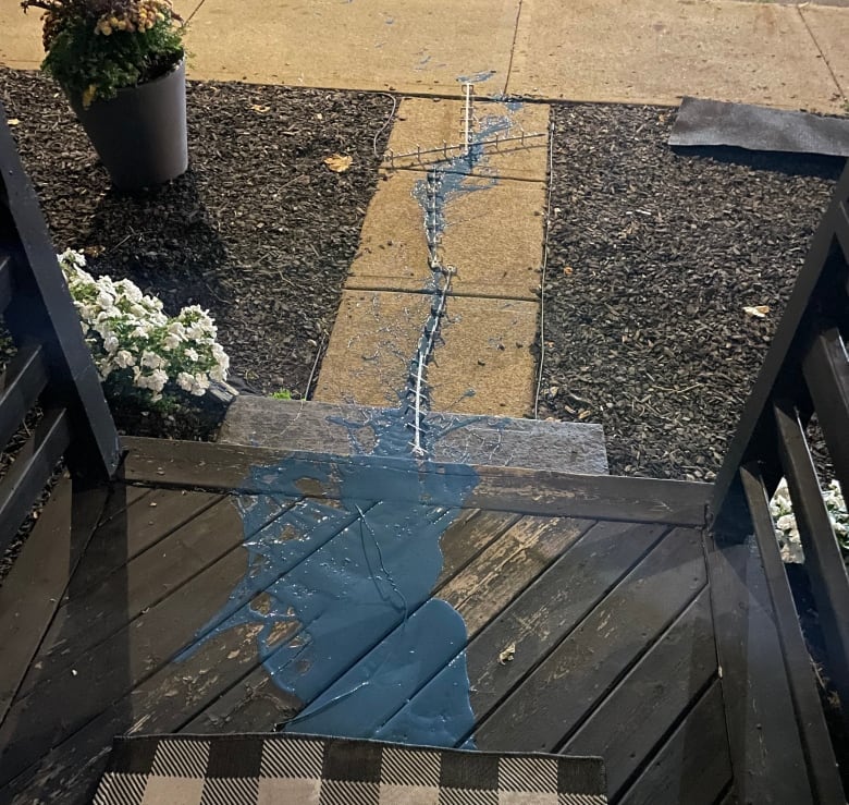 A walkway and porch with blue paint spilled on it and metal pieces shaped like a cross.