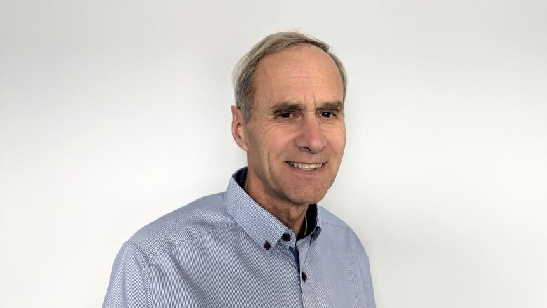 A man smiles while standing against a plain white background.