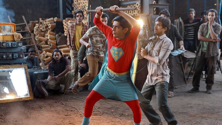 A man dressed like Superman is holding tool while a crowd watches.