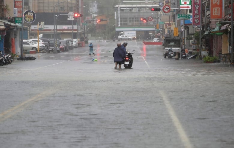 People push a motorbike through a flooded road